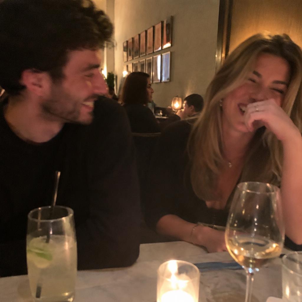 A couple laughing together at a candlelit restaurant table, a candid phone snapshot